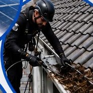 Technician clearing leaves from a gutter on a tiled roof